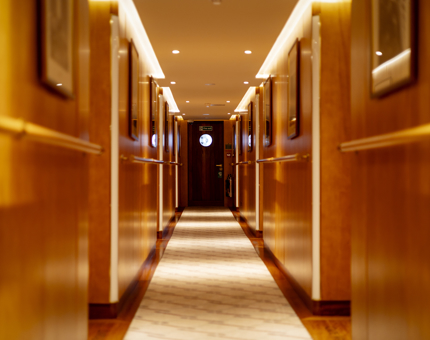 A corridor aboard Fingal Hotel in Edinburgh. There is a dark brown door at the end with a circular window.