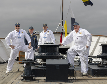 Four Royal Yachtsmen posing for a photo on the fo'c's'le, at the front of the ship. 