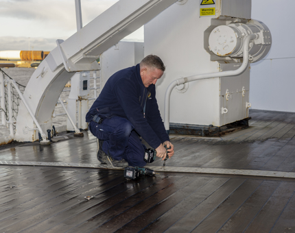On Britannia's deck, a Maintenance man is securing metal plates to the wood. 