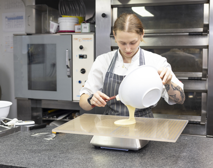 A Chef is in the Galley preparing tempered white chocolate to add to an Event dessert. 