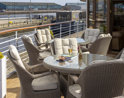 Aboard Fingal, there are tables and chairs set out on the deck in the sunshine, the Port of Leith is in the background. 
