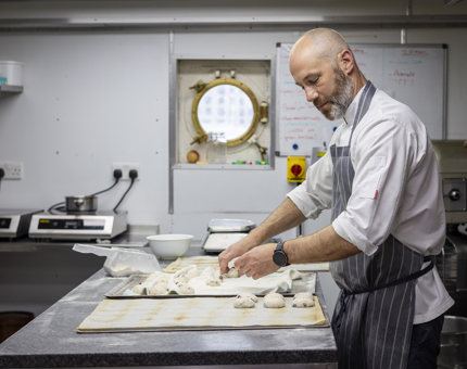 A chef is making bread rolls in the Galley. 