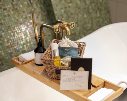A roll top bath with a bath tray across it, there are nice spa experience products on it. 