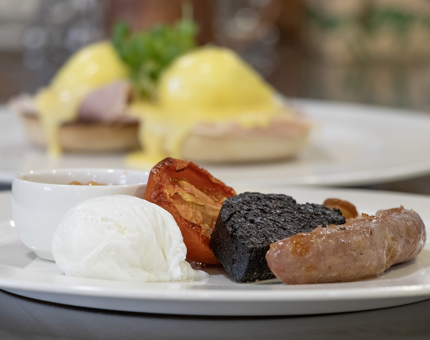 Plates with breakfasts on them. In the foreground there is a full cooked breakfast, in the background there us an eggs benedict. 