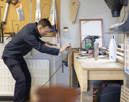 A maintenance team member is at a work bench, working on repairing a set of stairs. 