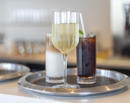 A tray with a glass of white wine, cuba libre and iced coffee. 