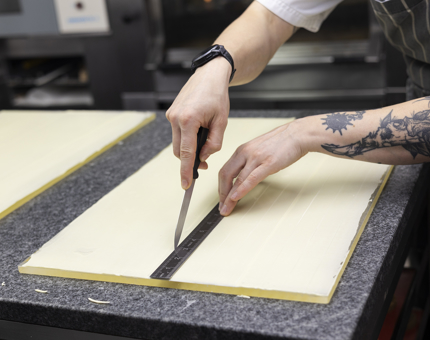 A Chef's hands are holding a knife and a ruler, cutting white chocolate pieces. 