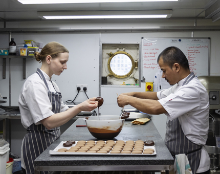 A woman and a man dipping desserts into chocolate in the Galley. 