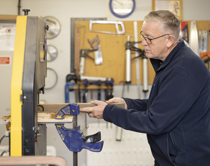 A man is cutting out pieces of wood in the workshop. 