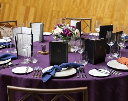 A close up of a table set for an evening event in Fingal's Ballroom. The table cloth is dark purple with dark blue napkins. 