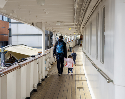 A man is walking along Britannia's Port side shelter deck with two small children. 