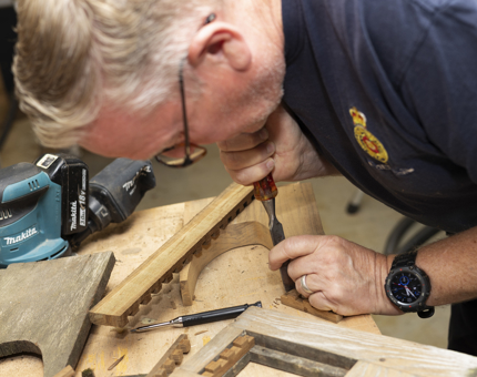 A maintenance man is using a chisel to work into a piece of wood. 