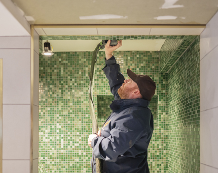 A man carrying out maintenance work in a green-tiled bathroom in Fingal's cabin. 