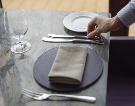 A close up of a hand laying cutlery on a table by the window in The Lighthouse Restaurant. 
