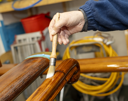 A close up of varnish being applied to a wooden handrail, The Royal Yacht Britannia. 