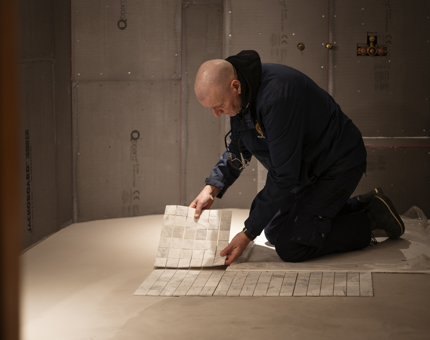A Maintenance man kneeling and tiling the floor of a bathroom aboard Fingal Hotel. 