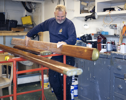 A maintenance man is sanding wooden handrails in the workshop. 