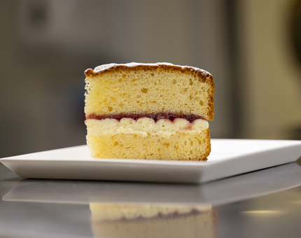 A slice of Victoria sponge cake on a white plate. 