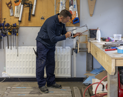 A man from the Maintenance team using a saw to cut wood in the workshop. 