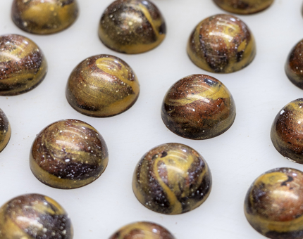A close up of a tray of whisky and orange bon bons. They are decorated with a gold swirl on top. 
