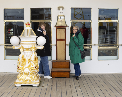 Two ladies pose for a photo by Britannia's Bell, listening to the audio guide handset. 