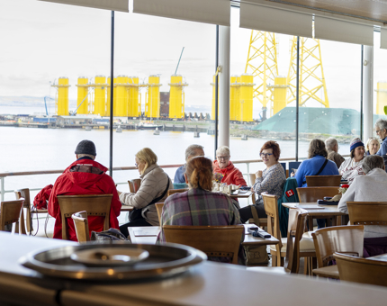 Visitors sitting at tables and enjoying the views over the Port of Leith in the Royal Deck Tearoom. 