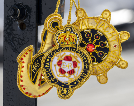 A close up of three embroidered hanging decorations. They are in the shape of an anchor, ships wheel and the Britannia crest. 