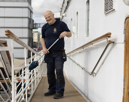 A Facilities Officer holding a duster cleaning the railings on Britannia's tour route.