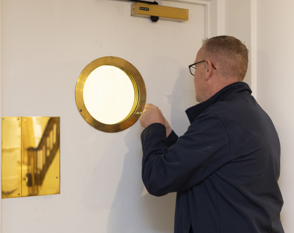 A Maintenance team member installing a porthole to a white door. 