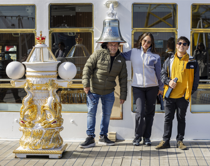 Three visitors are posing for a photo at The Royal Yacht Britannia's Bell on the Verandah Deck.