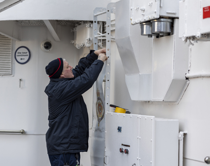 A Facilities Officer is repairing a banner aboard The Royal Yacht Britannia.  