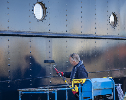 A man holding a paint roller applying paint to the side of Fingal. 