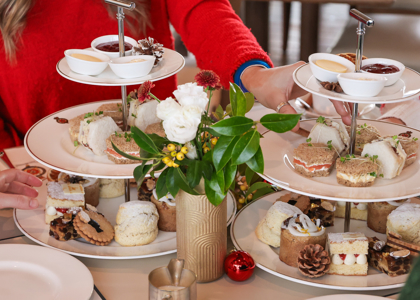 A hand reaching in to pick up a sandwich from an afternoon tea plate