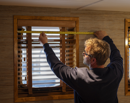 Aboard Fingal Hotel, a Maintenance team member is holding a tape measure, measuring a window for blinds. 