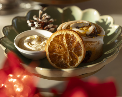 A close up of a plate with an iced cinnamon and mincemeat scone with brandy cream. 