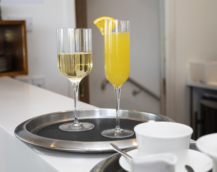 A glass of white wine and a mimosa are on a round silver tray on the bar in the Royal Deck Tearoom. 
