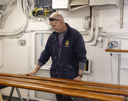In the workshop, Maintenance team member is sanding wooden handrails.