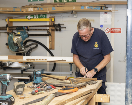 A maintenance man is at a workbench restoring scupper boards. 
