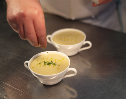 A chef is sprinkling chives onto two bowls of cullen skink soup in Britannia's Galley. 