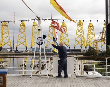 A Facilities Officer Cleaning The Railings On The Verandah Deck, with yellow structures in the background in the Port of Leith. 