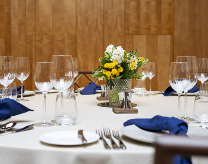 A table in Fingal's Ballroom set for a dinner. There are blue napkins and a vase with yellow and white flowers. 