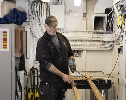 A Maintenance man using a heat gun to remove varnish from hand rails