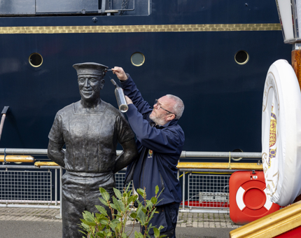 A Facilities Officer is Cleaning A Statue of a Royal Yachtsman With Blow Torch And Wire Brush On Britannia'S Quayside