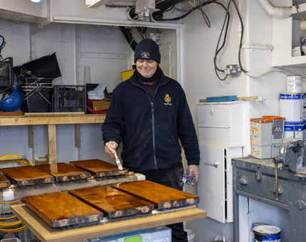 A Maintenance man holding a paintbrush varnishing wooden steps from the Bridge. 