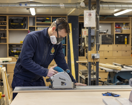 A maintenance man is cutting wood to make shelves for the Shop's storage room aboard Britannia. 