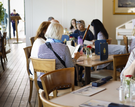 Visitors sitting at the tables, enjoying delicious food and drinks in the Royal Deck Tearoom aboard Britannia. 