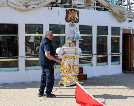 On the Verandah Deck, a Maintenance team member is pulling a rope straight that has a red dress flag attached to it. 