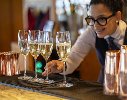 A Hospitality Server is preparing glasses of Champagne to be served at The Lighthouse Restaurant & Bar. 