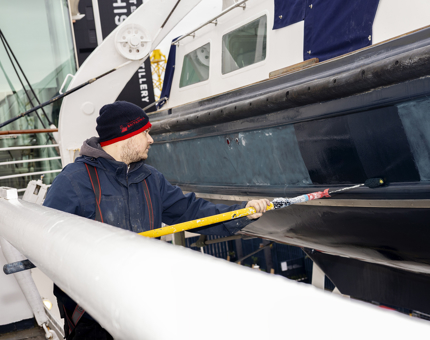 A Maintenance man is Painting The Fast Motor Launch boat with a long paint roller. 