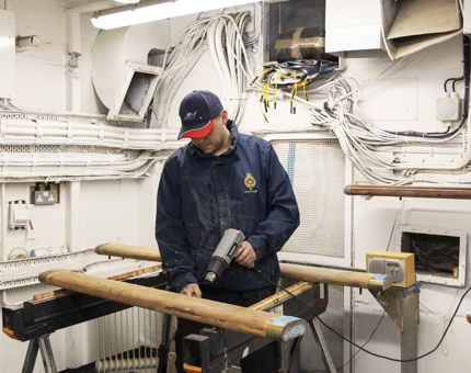 A maintenance team member is removing varnish from handrails using a heat gun